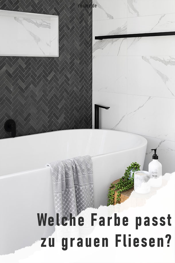 Einblick in ein minimalistisches Badezimmer mit weiß-mamorierten Fliesen an der rechten Wand und grauen Fliesen in Fischgrät-Optik an der linken Wand. Die Badewanne ist mit schwarzer Armatur gesäumt. Daneben befindet sich ein brauner Hocker mit Pflanze, Kerze und Duschbad. Das Bild ist in der rechten unteren Ecke abgerissen und zeigt den Titel: Welche Farbe passt zu grauen Fliesen?
