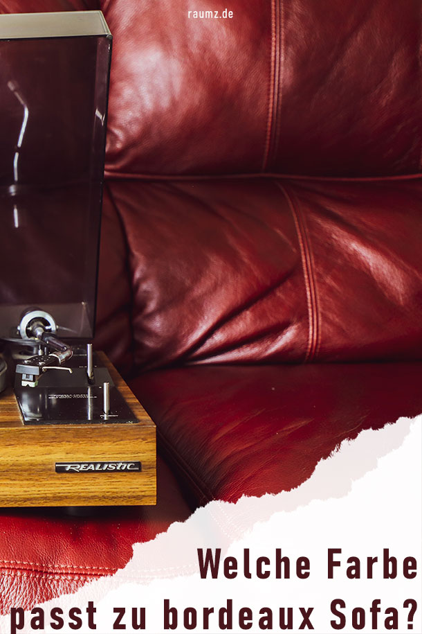 Hochformatiges Bild über das Thema "Welche Farbe passt zu bordeaux Sofa?". Zu sehen ist ein bordeauxfarbenes Sofa aus Leder. Daneben befindet sich ein Tischchen aus Nussbaumholz. Darauf befindet sich ein Plattenspieler aus gleichem Holz und silbernen Akzenten.