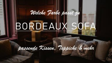 Titelbild zu dem Thema "Welche Farbe passt zu bordeaux Sofa?". Darauf abgebildet ist ein Ausschnitt eines Wohnzimmers mit zwei bordeauxfarbenen Sofas. Auf dem linken Sofa ist ein senfgelbes Kissen drapiert. Auf dem rechten Sofa befinden sich mehrere Kissen aus beige oder blaugemustertem Stoff. Die Wände sind in dunkelbraunem Holz vertäfelt.