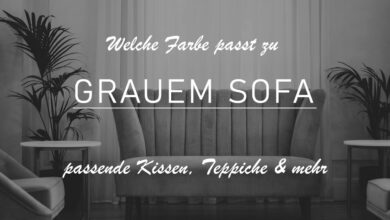 Titelbild des Beitrags "Welche Farbe passt zu grauem Sofa?" mit einem Einblick in ein Wohnzimmer. Zu sehen ist ein graues Sofa mit schwarzen Füßen im Stil der 1920er. Das Sofa ist mit zwei Beistelltischchen und einem Sessel umringt. Links und rechts sind zusätzlich Pflanzen aufgestellt. Das graue Sofa steht vor einem Fenster mit semi-transparentem Vorhängen.