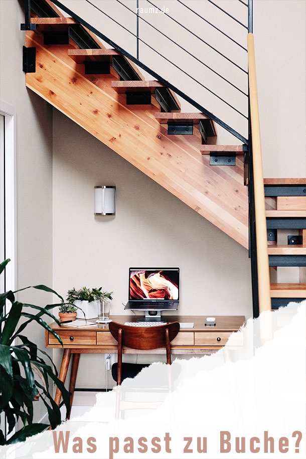 Bild im Hochformat. Zu sehen ist ein Treppenflur mit einer Treppe aus Buchenholz. Darunter befindet sich ein kleiner Schreibtisch bzw. ein Arbeitsplatz. Der Schreibtisch ist auch Buchenholz gefertigt und mit grünen Pflanzen und silbernen Dekorelementen versehen. Das Treppengeländer ist in schwarz gehalten. Die recht untere Ecke ist abgerissen und man erkennt den Titel: Was passt zu Buche?