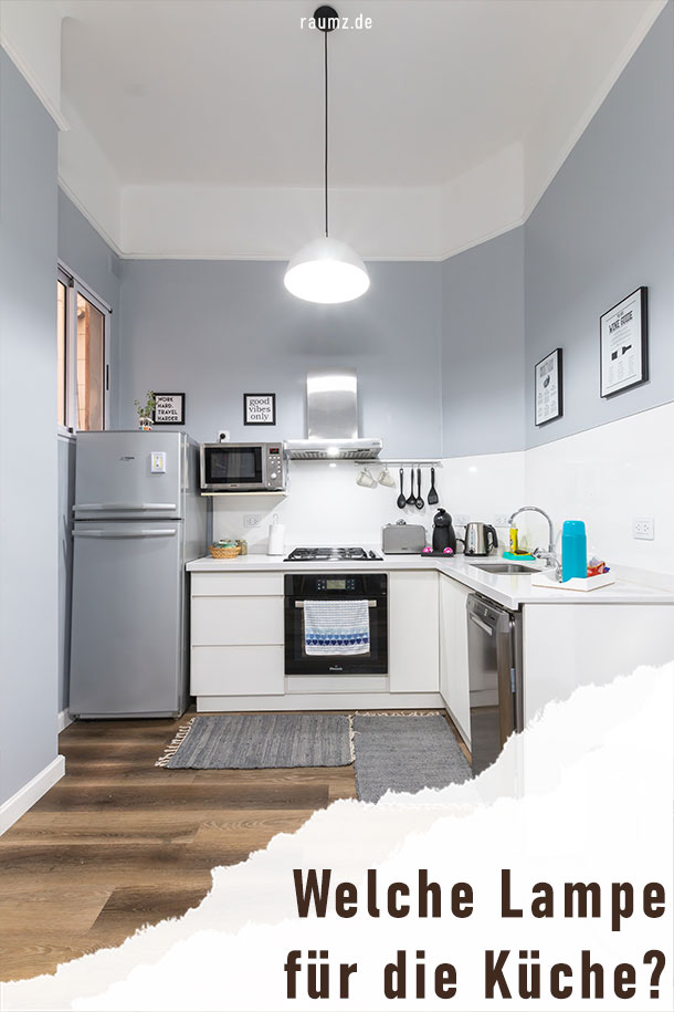 Einblick in eine Küche. Die Küche ist mit hellem Blaugrau koloriert. Zusätzlich ist eine Deckenlampe angebracht, womit die ganze Küche ausgeleuchtet wird. Weiterhin befindet sich an der Abzugshaube eine weitere Lampe. Aufgrund der hellen Farbe, der großen Beleuchtung und der weißen Küche ist der Eindruck sehr freundlich und weit. 